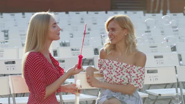 Two Attractive Beautiful Young Blond Women Blow Bubbles in the Park and are Happy on Sunset