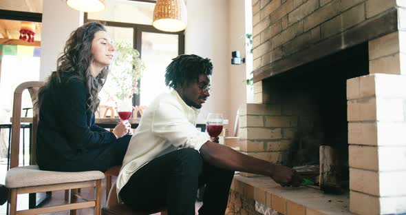 Young Couple Sit with Glass of Wine in Front of Fireplace