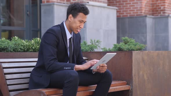 Excited African Businessman Celebrating Success on Tablet Sitting on Bench