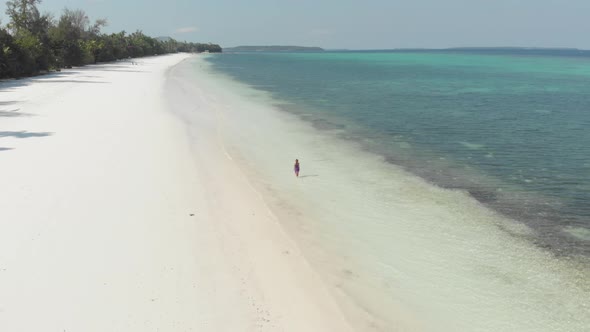 Aerial: woman walking on white sand tropical beach turquoise water coral reef