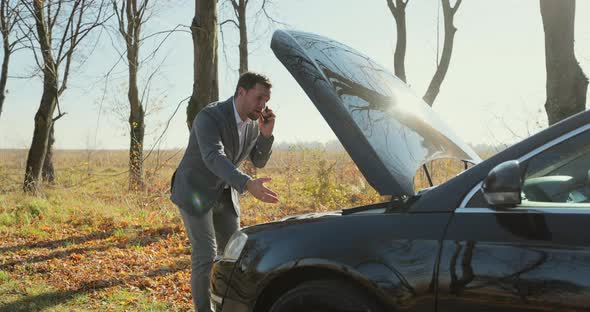 Desperate Businessman Standing and Speak on Phone Near the Broken Car Opened the Hood Road Help