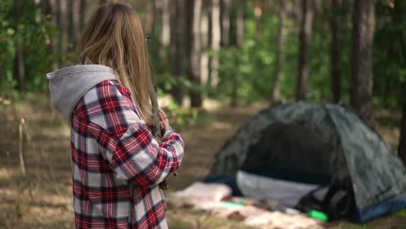 Positive Beautiful Woman Looking Back at Camp Tent Standing with Firewood Branches Gesturing Thumb