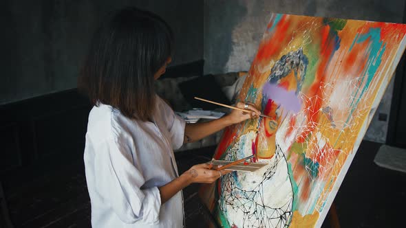 Young Woman Artist is Painting a Portrait on Canvas in Modern Art Style While Working in Studio