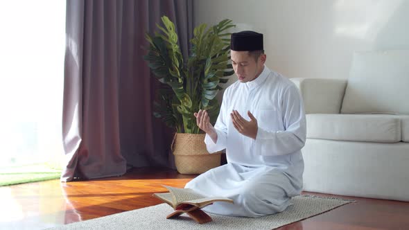 Young Muslim man wearing Islamic clothes reading Quran and praying