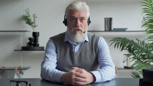 An Elderly Businessman in a Headset Having a Video Conference with a Business Partner Working in an