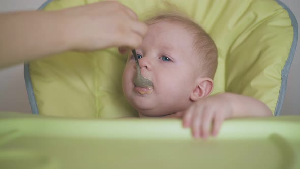 Baby Eats Meal with Appetite Sitting in Highchair Closeup