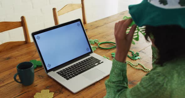Mixed race woman in green glasses and costume having a video call on laptop at home