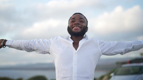 Happy Cheerful Handsome African American Gay Man Taking Off Hat Stretching Hands at Sunset on Resort