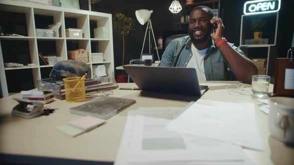 Smiling African Businessman Talking Cellphone in Dark Coworking.