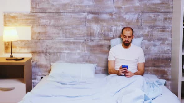 Guy Browsing on Smartphone in His Bed