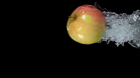 An Apple is Bouncing Horizontally From Water with Splashes on a Black Background