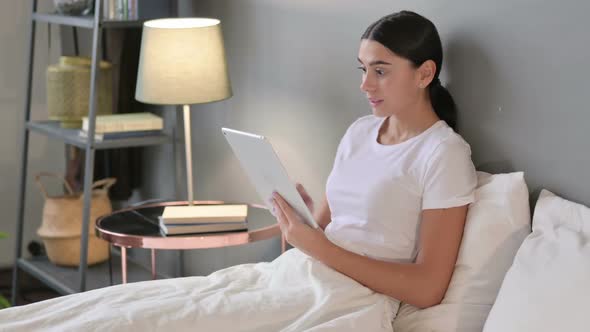 Excited Latin Woman Celebrating on Tablet in Bed