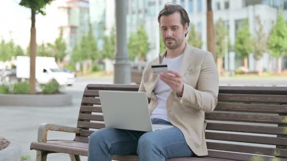 Excited Young Man Shopping Online with Laptop Outdoor