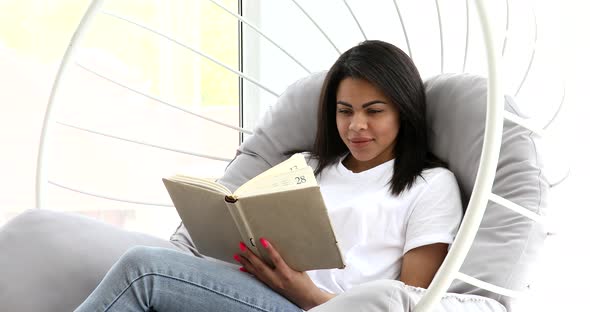 Young black woman reading interesting developing book at home.