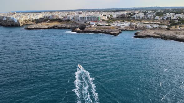 Aerial drone shot of a motorboat headed to Polignano A Mare, Italy.