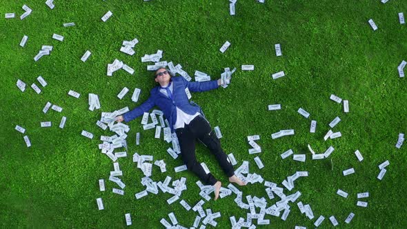 Young Man Businessman or Student or Office Worker Lies on a Green Grassy Lawn Strewn with Money