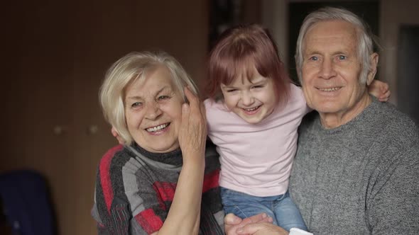 Granddaughter Kissing Senior Smiling Grandfather with Grandmother at Home