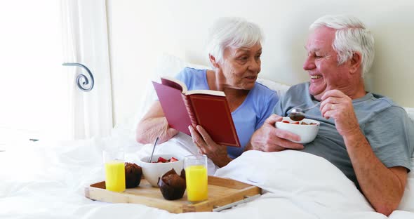 Senior couple interacting with each other while having breakfast on bed