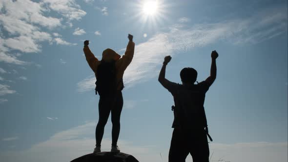 Silhouette of a successful Asian couple raising their arms on top of a mountain enjoying the valley.