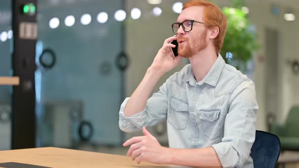Cheerful Casual Redhead Man Talking on Smartphone in Office 