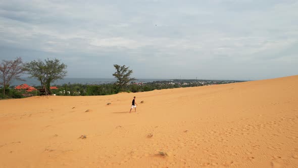 man walking up a desert sand dune along the ocean coast of Mui Ne Vietnam