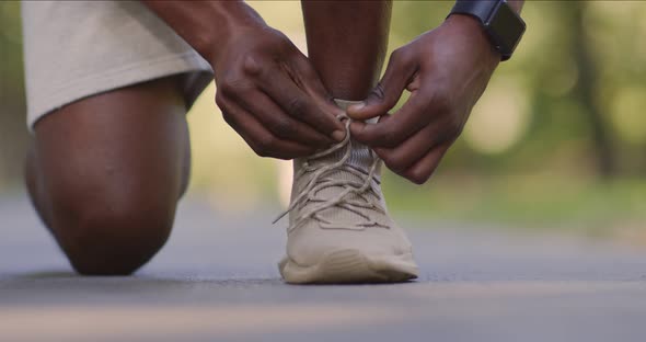 Closeup of Black Guy in Sportswear Tying His Sneakers Shoelaces Before Jogging Outdoors