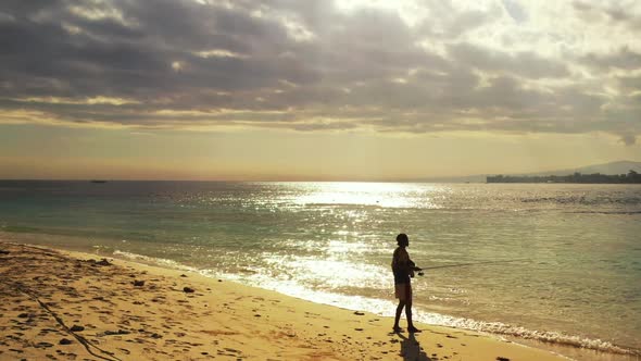 One boy fishing alone on tropical island beach lifestyle by blue green water with white sandy backgr