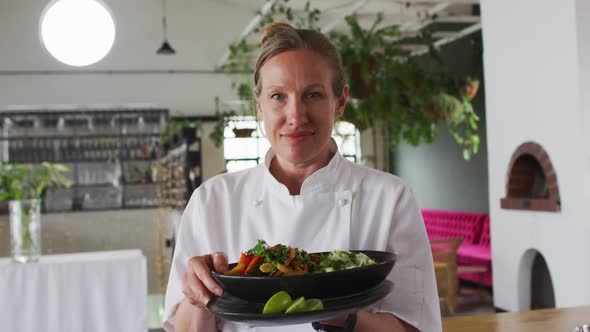 Caucasian female chef preparing a dish and smiling in a kitchen