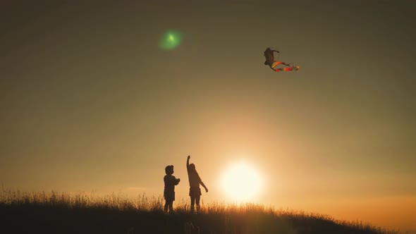 Two Children Launch a Kite in the Field at Sunset