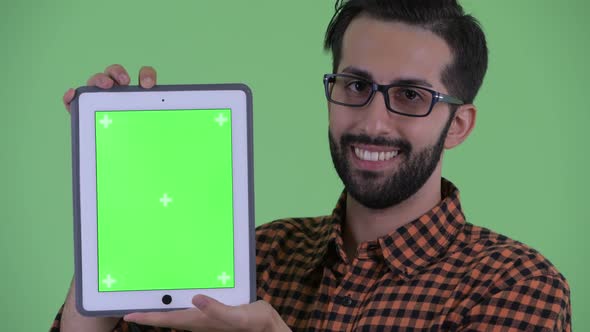 Face of Happy Young Bearded Persian Hipster Man Talking While Showing Digital Tablet