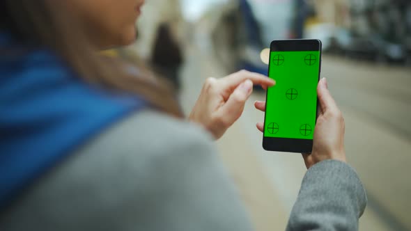 Woman at the Street Using Smartphone with Green Mockup Screen in Vertical Mode Against the Backdrop