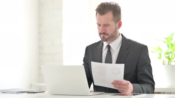 Young Businessman with Laptop Having Loss While Reading Documents