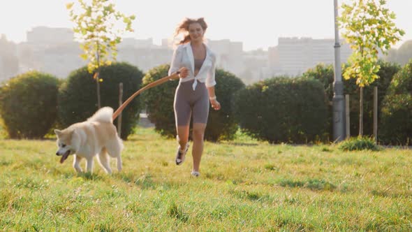 Young woman walking her cute Akita Inu dog in park on sunny day. Lovely pet