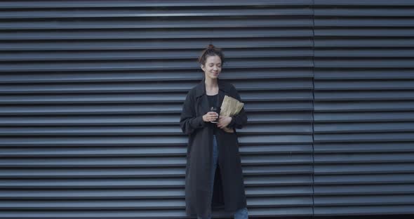 Smiling Woman Standing at Black Rolling Shutter Background with Craft Paper-bag and Coffee. Portrait