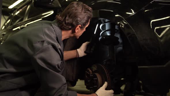 Auto mechanic man standing at the opened hood and lighting with lamp while working at the workshop