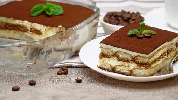 Portion of Traditional Italian Tiramisu dessert and baking dish on grey concrete background