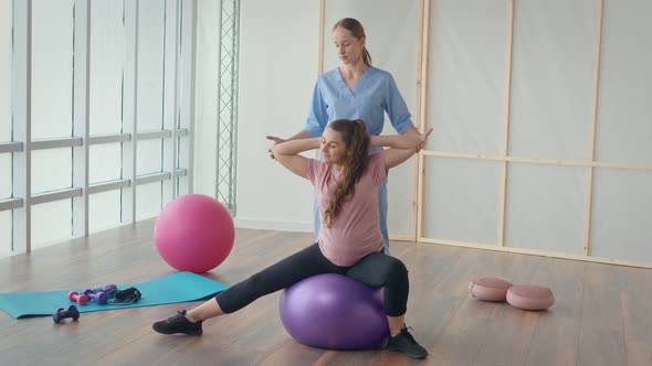 Medical Worker Helping Pregnant Woman to Do Ball Exercises