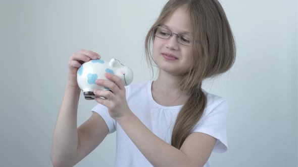 Little Girl Wearing Glasses Putting Coins Into Cow Piggy Bank