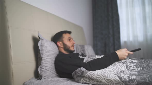 Sick Man Lying Bed Watching TV Switching Channels with Remote