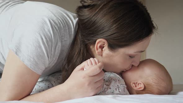 Happy Mother Kisses Plump Cheeks of Newborn Daughter