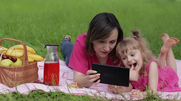 Family Weekend Picnic. Daughter Child Girl with Mother Play Online Games on Tablet. Chatting