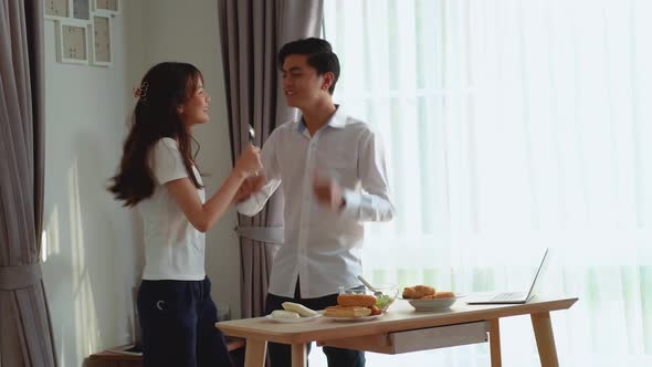 Young happy active asian couple dancing laughing together preparing food at home
