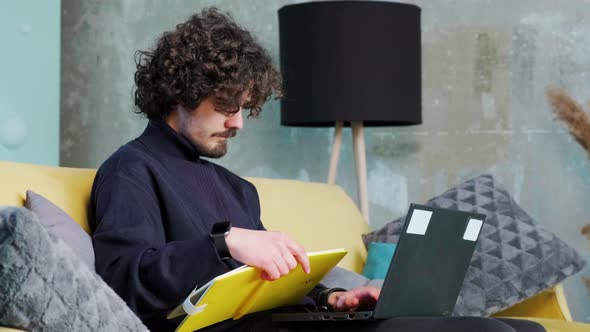 Young Man is Browsing at His Laptop and Writing Notice on His Paper Notebook