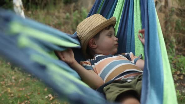 Happy kid boy in hammock in summer garden