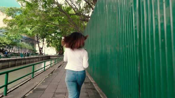 Young Asian woman walking on the street and listening to music in headphones.