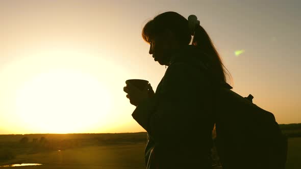 Silhouette Woman Traveler, Stands on Top of a Hill Drinking Coffee in Glass From Thermos. Tourist