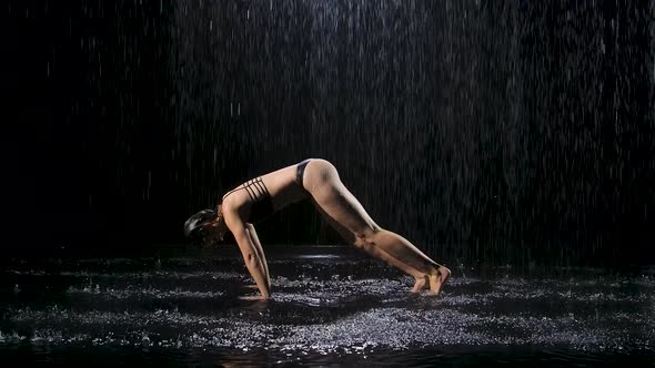 Woman in the Rain Practices Yoga Performing Asanas. Downward Facing Dog Pose with Bent Leg