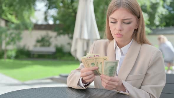 Upset Young Businesswoman Counting Dollars in Outdoor Cafe