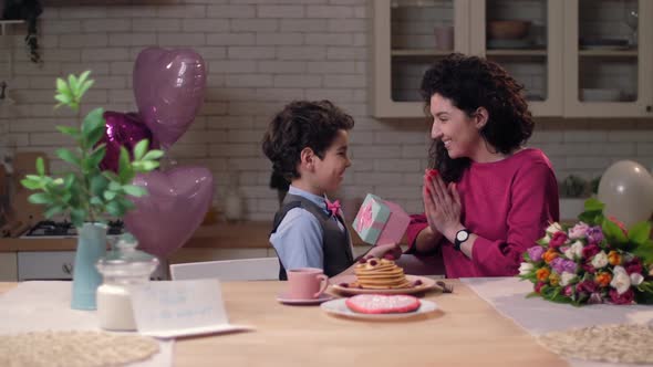 Cute Son Presenting Gift Box To Surprised Mom