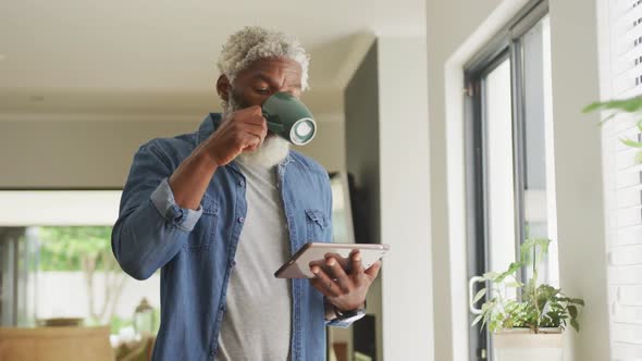 Video of african american senior man drinking coffee and using tablet